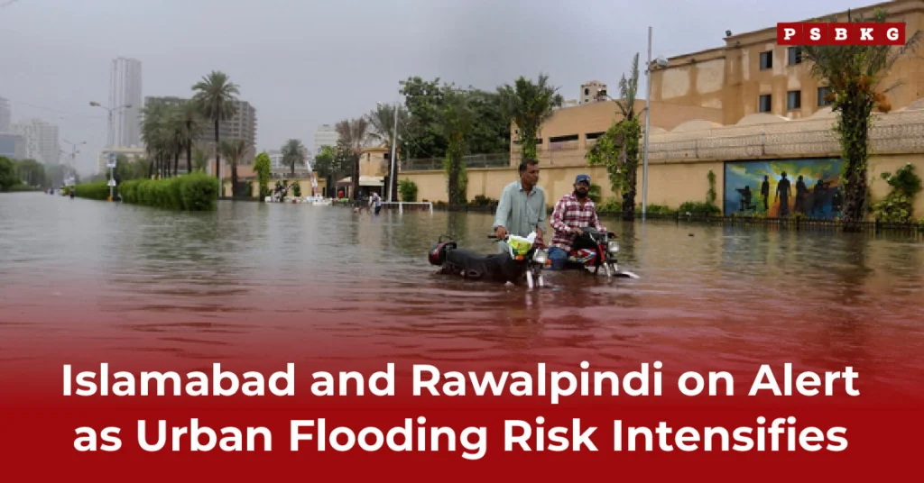 Two men navigate a flooded street on a motorcycle during urban flooding, with submerged buildings and palm trees around them under a gray, overcast sky.