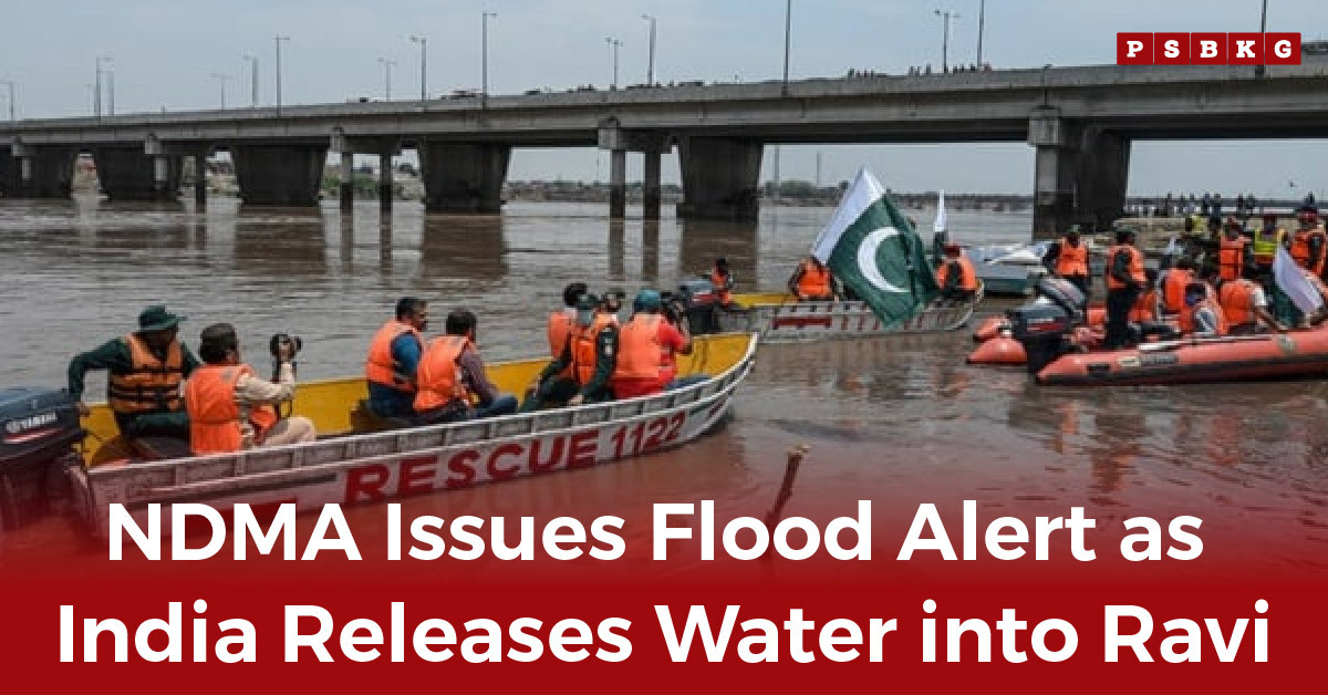 Rescue boats with people in orange vests navigate a flooded river under a bridge, a Pakistani flag waving nearby, during the Pakistan Flood Alert Ravi issued by NDMA.