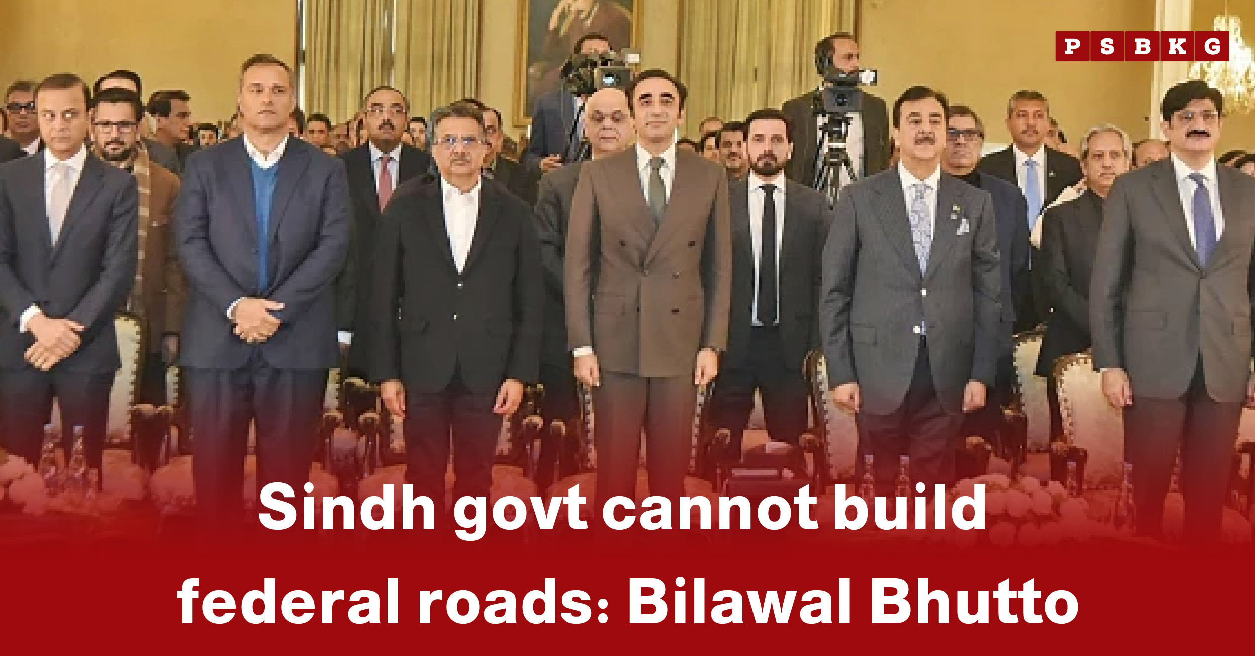 A group of men in formal attire stands together with cameras and a backdrop, highlighting Sindh government federal roads at a political event.