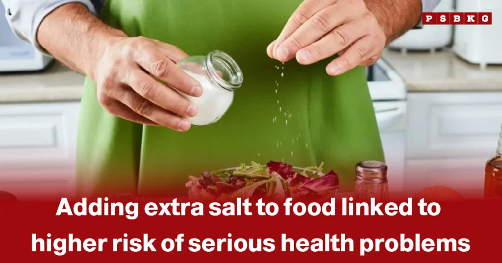 extra salt health risks: A person in a green apron adds salt to a salad in a kitchen, highlighting the health risks of excessive salt consumption.
