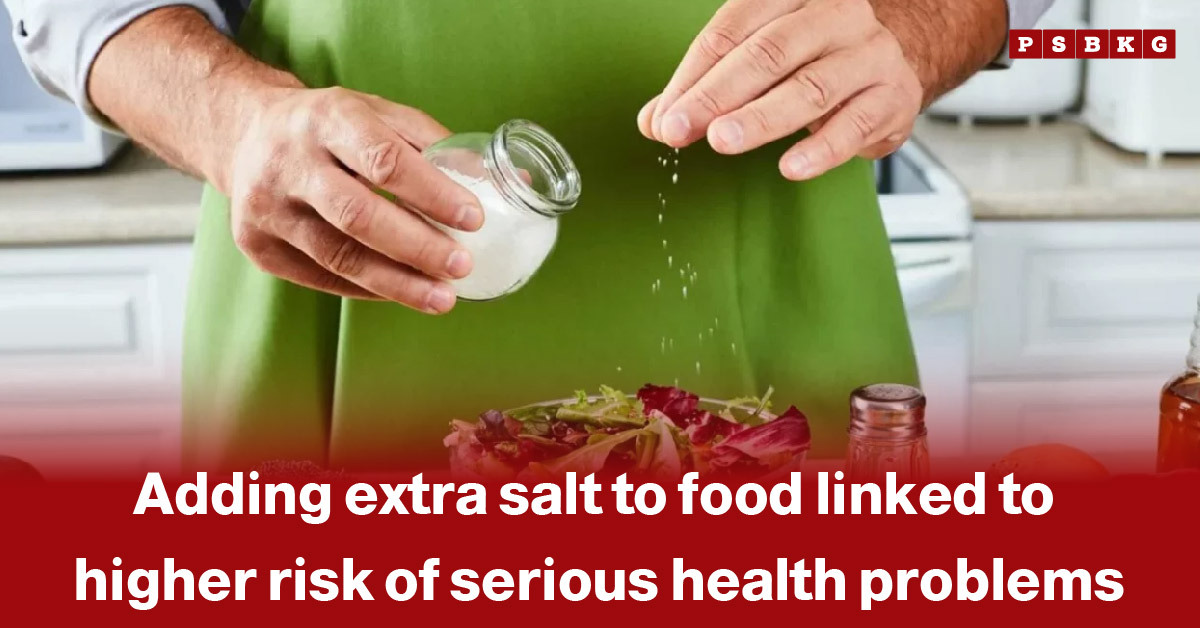 extra salt health risks: A person in a green apron adds salt to a salad in a kitchen, highlighting the health risks of excessive salt consumption.
